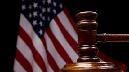  A wooden table features a judge's gavel, positioned in front of an American flag, representing the legal system and governance.