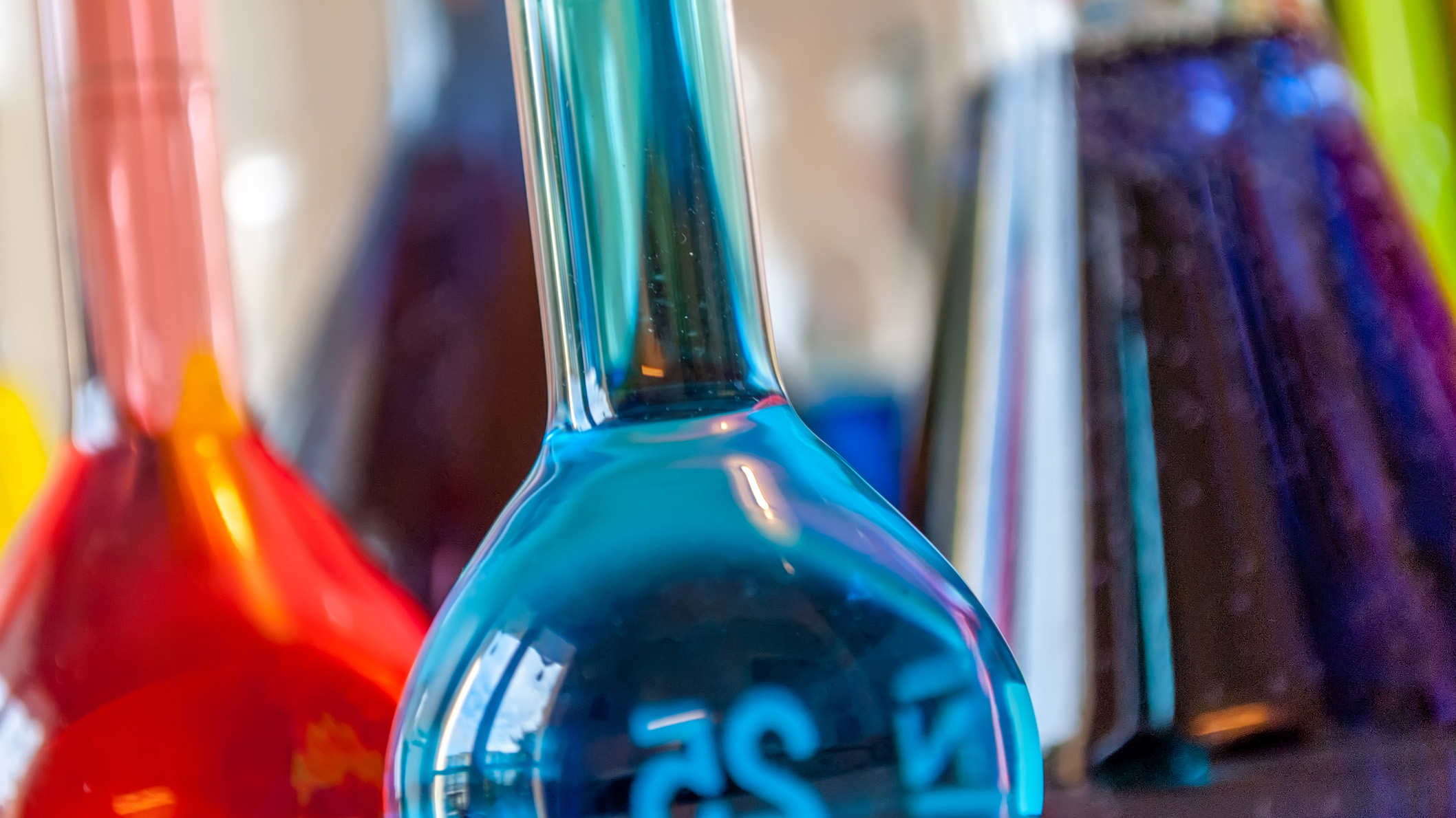 Blue liquid in a glass container with red liquid in a glass container in the background.